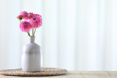 Photo of Beautiful pink flowers in vase on wooden table at home. Space for text