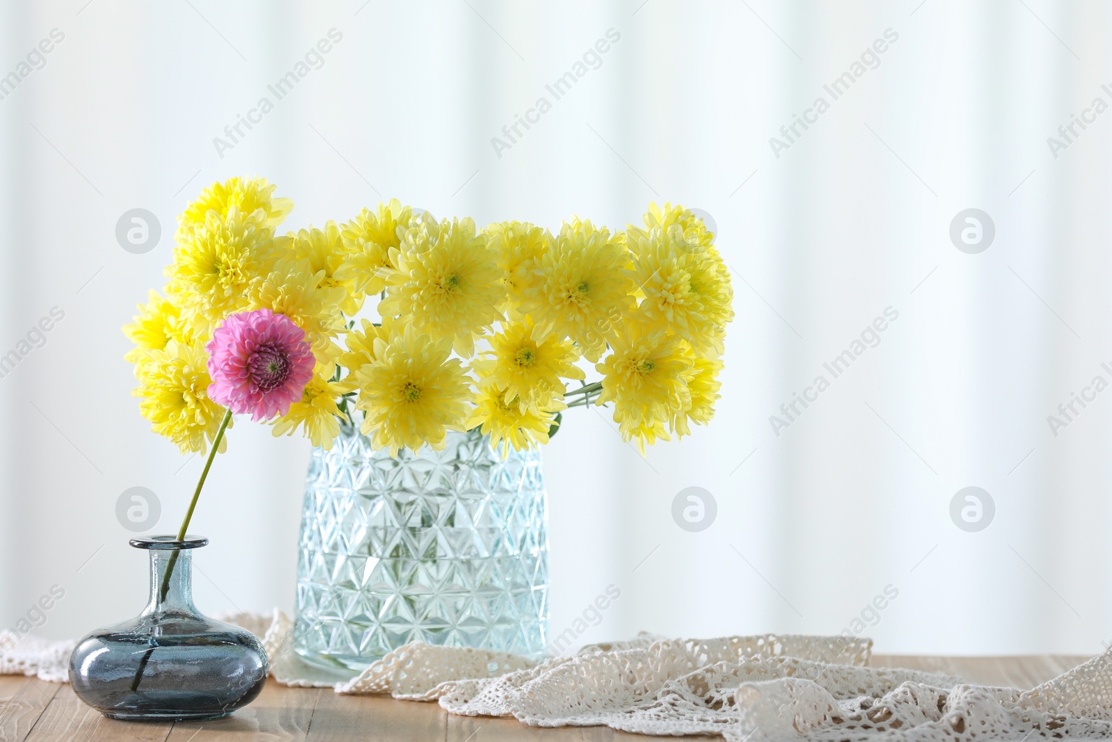 Photo of Beautiful yellow and pink flowers in vases on wooden table at home. Space for text