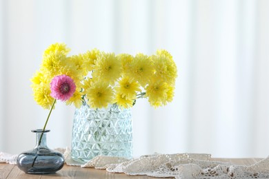 Photo of Beautiful yellow and pink flowers in vases on wooden table at home. Space for text