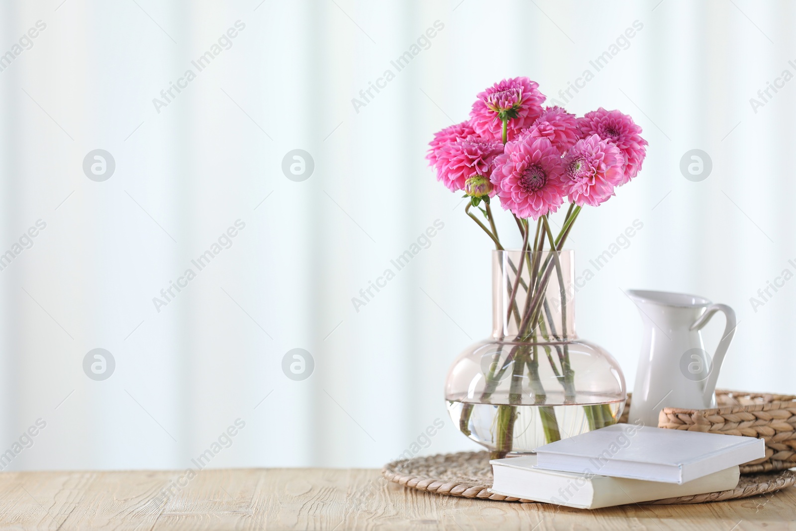 Beautiful pink flowers in vase and books on wooden table at home. Space for text Photo of Beautiful pink flowers in vase and books on wooden table at home. Space for text