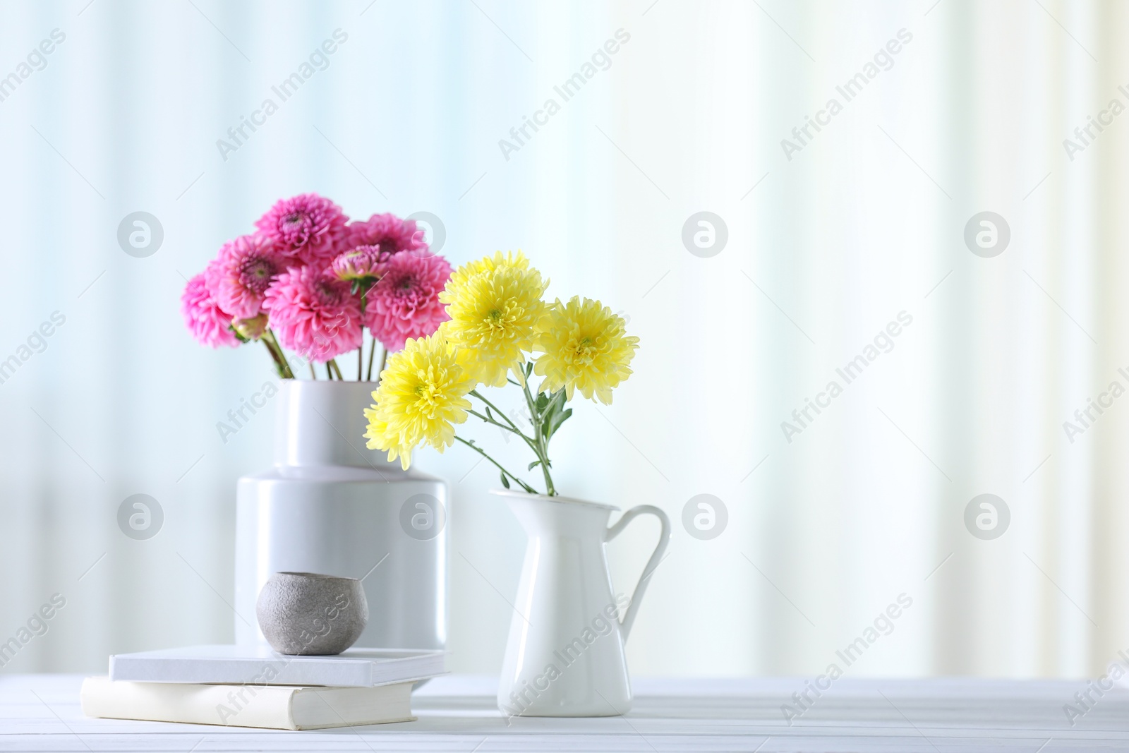 Photo of Beautiful flowers in vases and books on white wooden table at home. Space for text