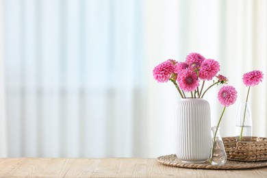 Photo of Beautiful pink flowers in vases on wooden table at home. Space for text