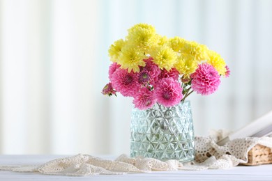 Photo of Beautiful yellow and pink flowers in vase on white wooden table at home. Space for text