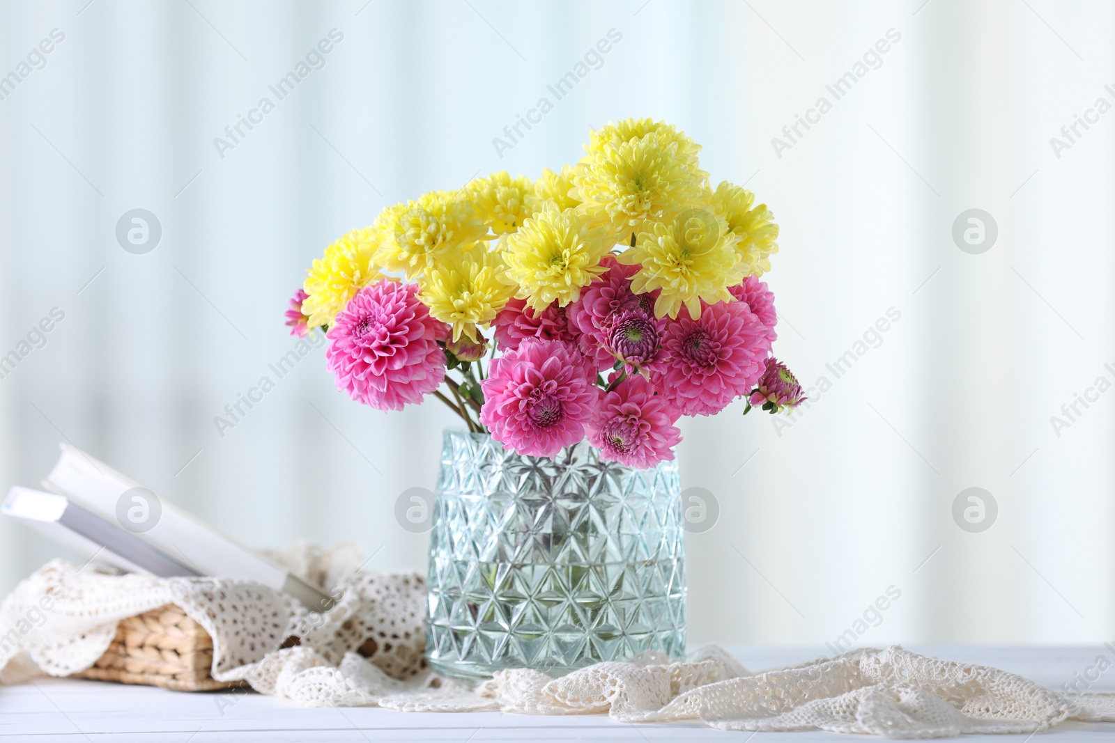 Photo of Beautiful yellow and pink flowers in vase on white wooden table at home