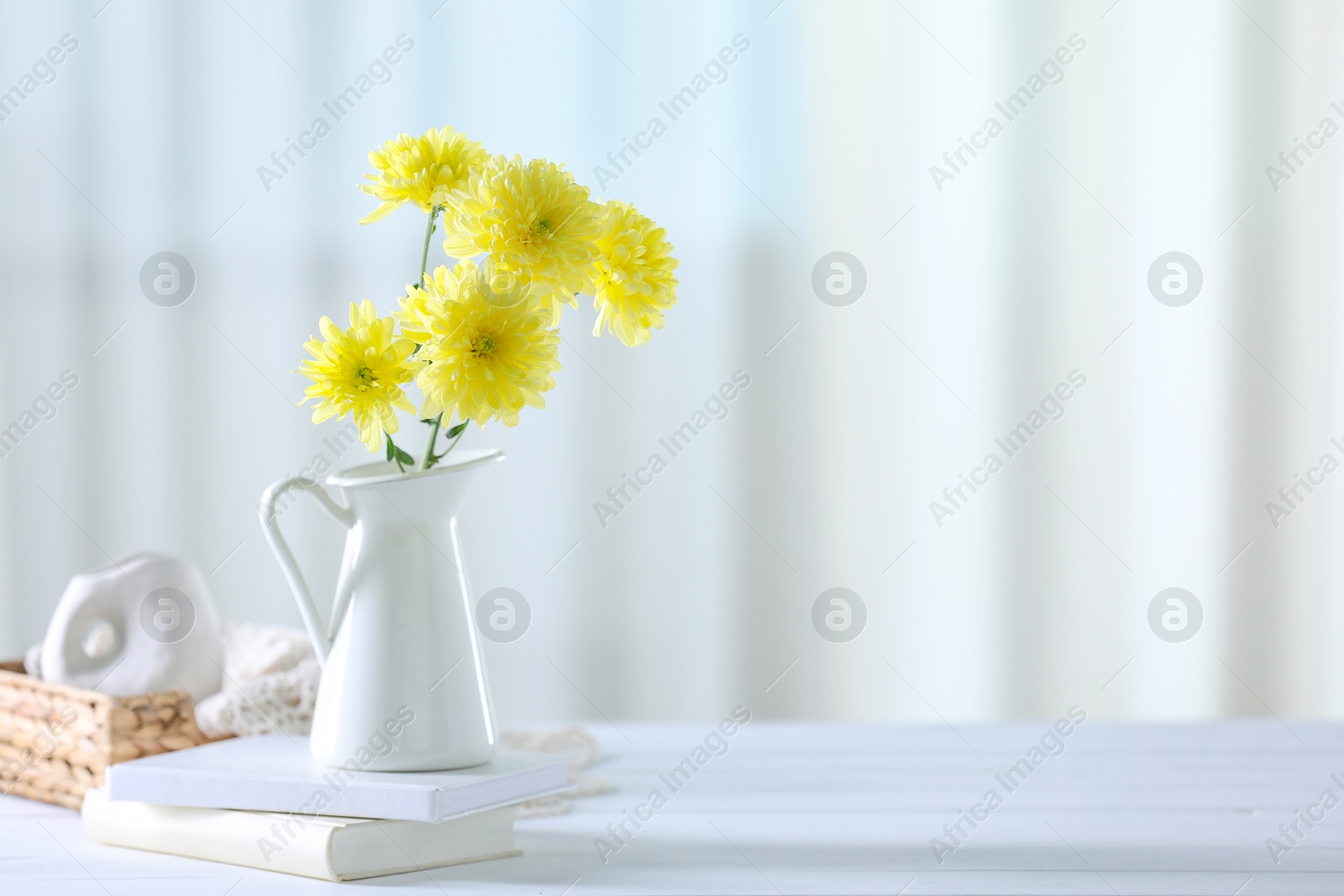 Photo of Beautiful yellow flowers in vase and books on white wooden table at home. Space for text