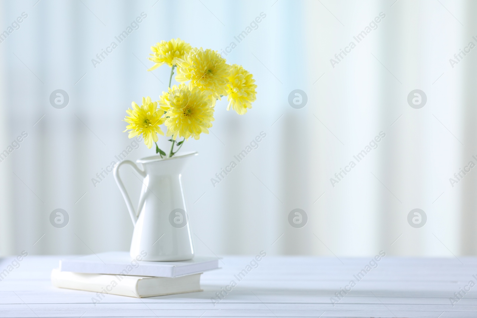 Photo of Beautiful yellow flowers in vase and books on white wooden table at home. Space for text