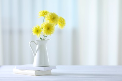 Photo of Beautiful yellow flowers in vase and books on white wooden table at home. Space for text