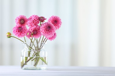 Photo of Beautiful pink flowers in vase on white wooden table at home. Space for text