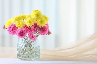 Photo of Beautiful flowers in vase and beige tulle fabric on white wooden table at home. Space for text