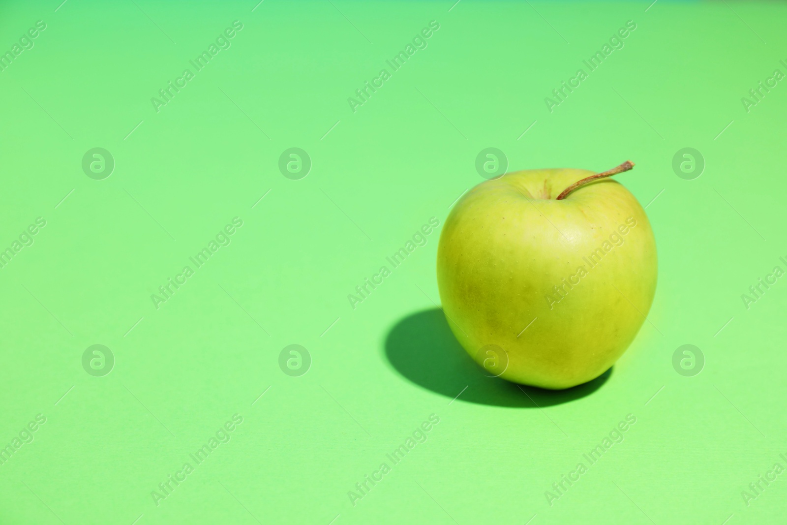 Photo of Fresh ripe apple on light green background, space for text