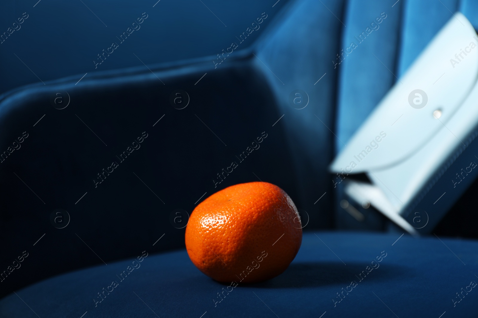 Photo of Fresh ripe tangerine on dark blue armchair