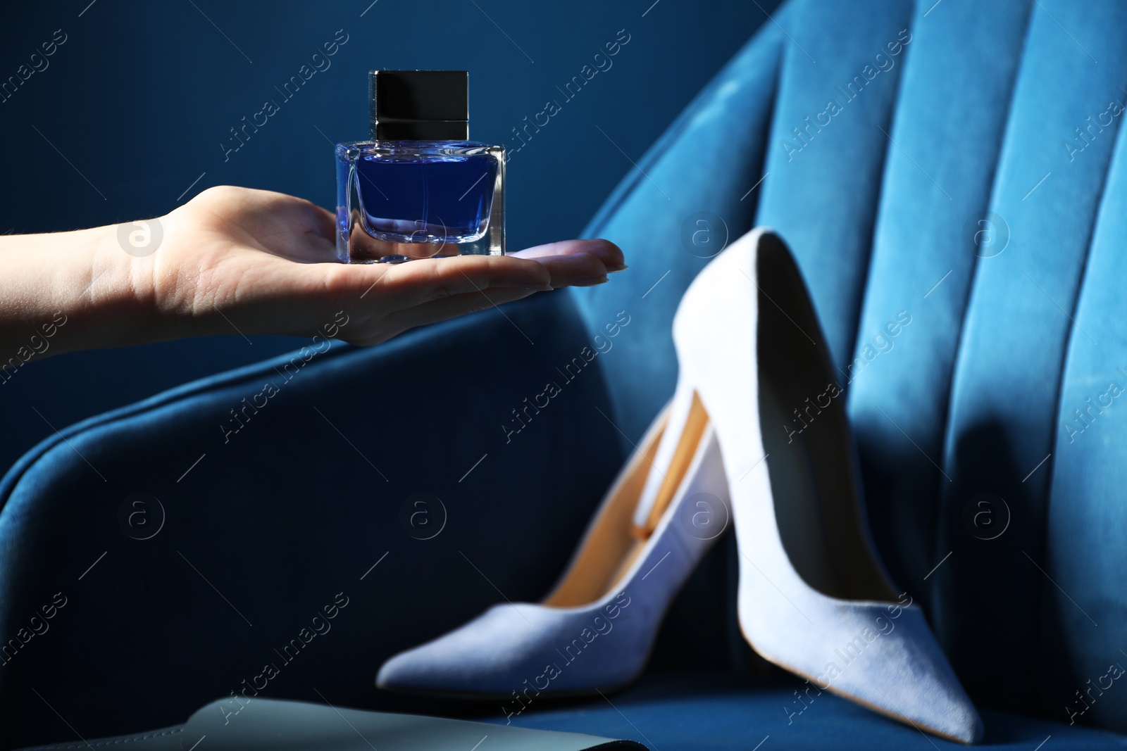 Photo of Woman holding bottle of perfume near armchair with high-heeled shoes, closeup