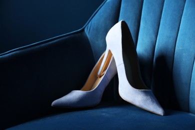 Photo of Light steel blue high-heeled shoes on dark blue armchair, closeup