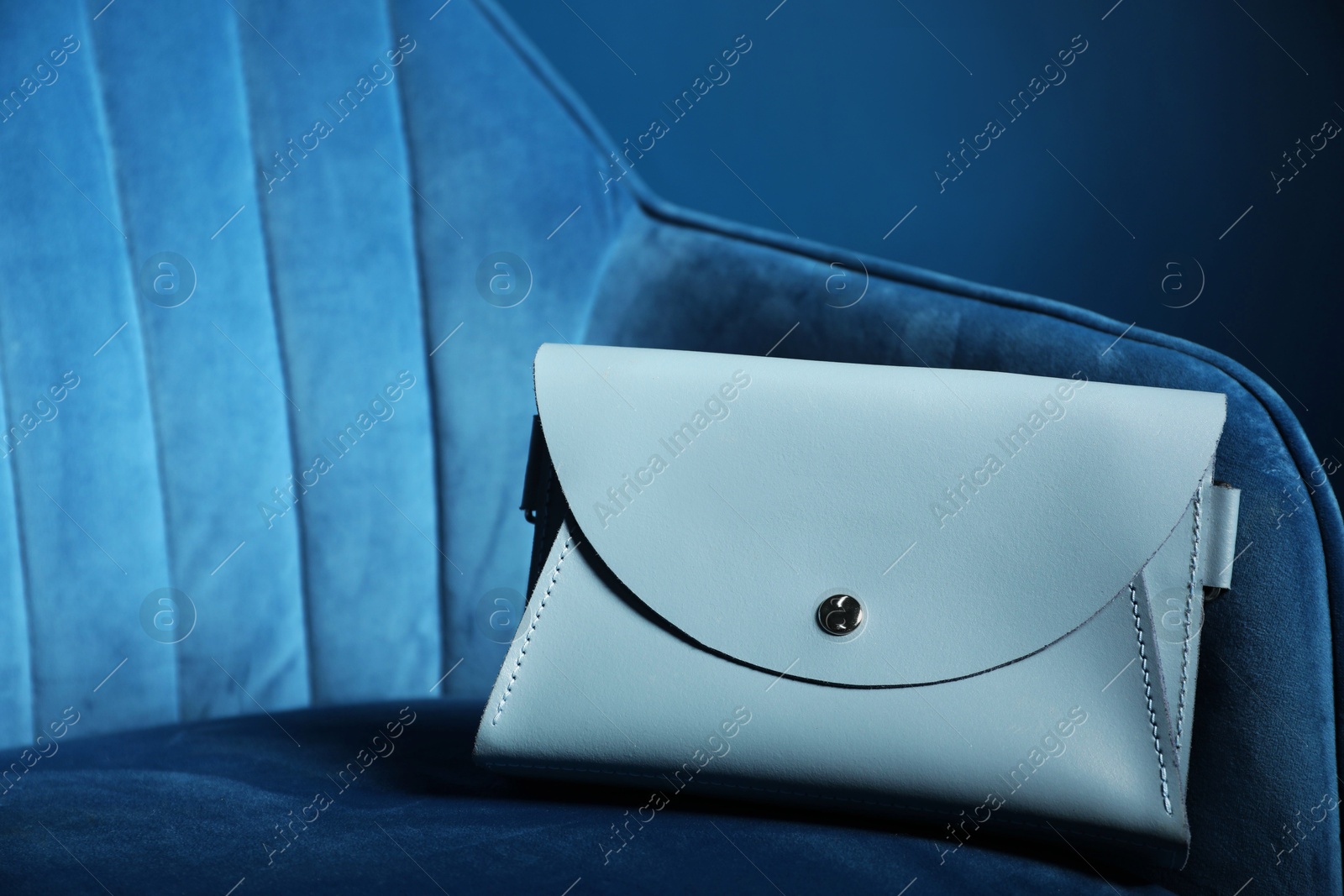 Photo of Stylish clutch on dark blue armchair, space for text