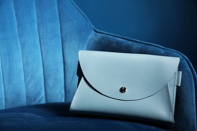 Photo of Stylish clutch on dark blue armchair, space for text