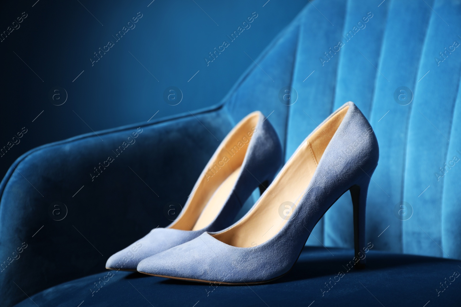 Photo of Light steel blue high-heeled shoes on dark blue armchair, closeup