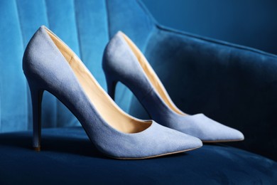 Photo of Light steel blue high-heeled shoes on dark blue armchair, closeup