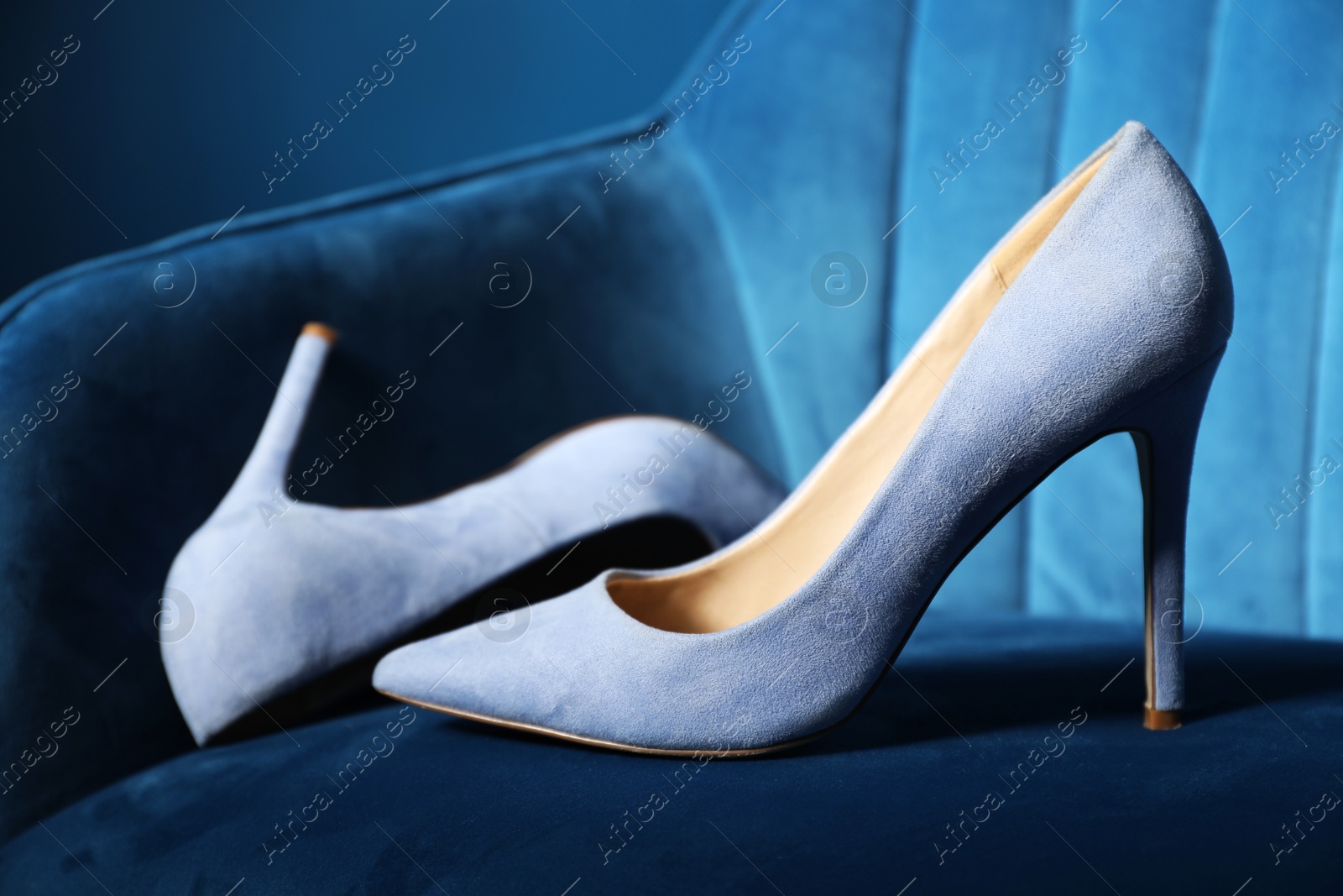 Photo of Light steel blue high-heeled shoes on dark blue armchair, closeup