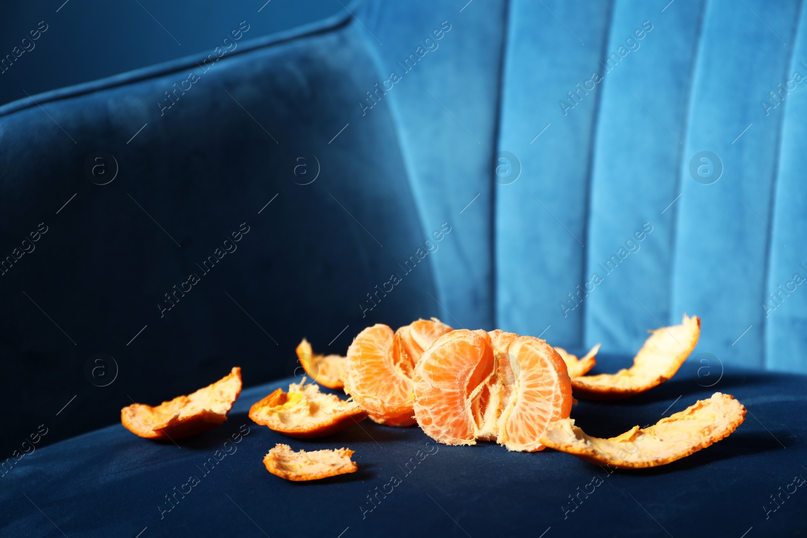 Photo of Fresh peeled tangerine on dark blue armchair