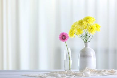 Photo of Beautiful yellow and pink flowers in vases on white wooden table at home. Space for text