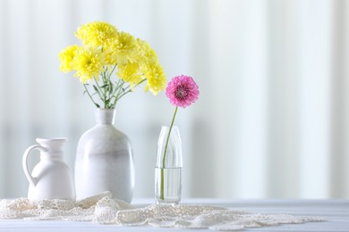 Photo of Beautiful yellow and pink flowers in vases on white wooden table at home. Space for text