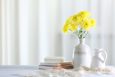 Photo of Beautiful yellow flowers in vase and books on white wooden table at home. Space for text