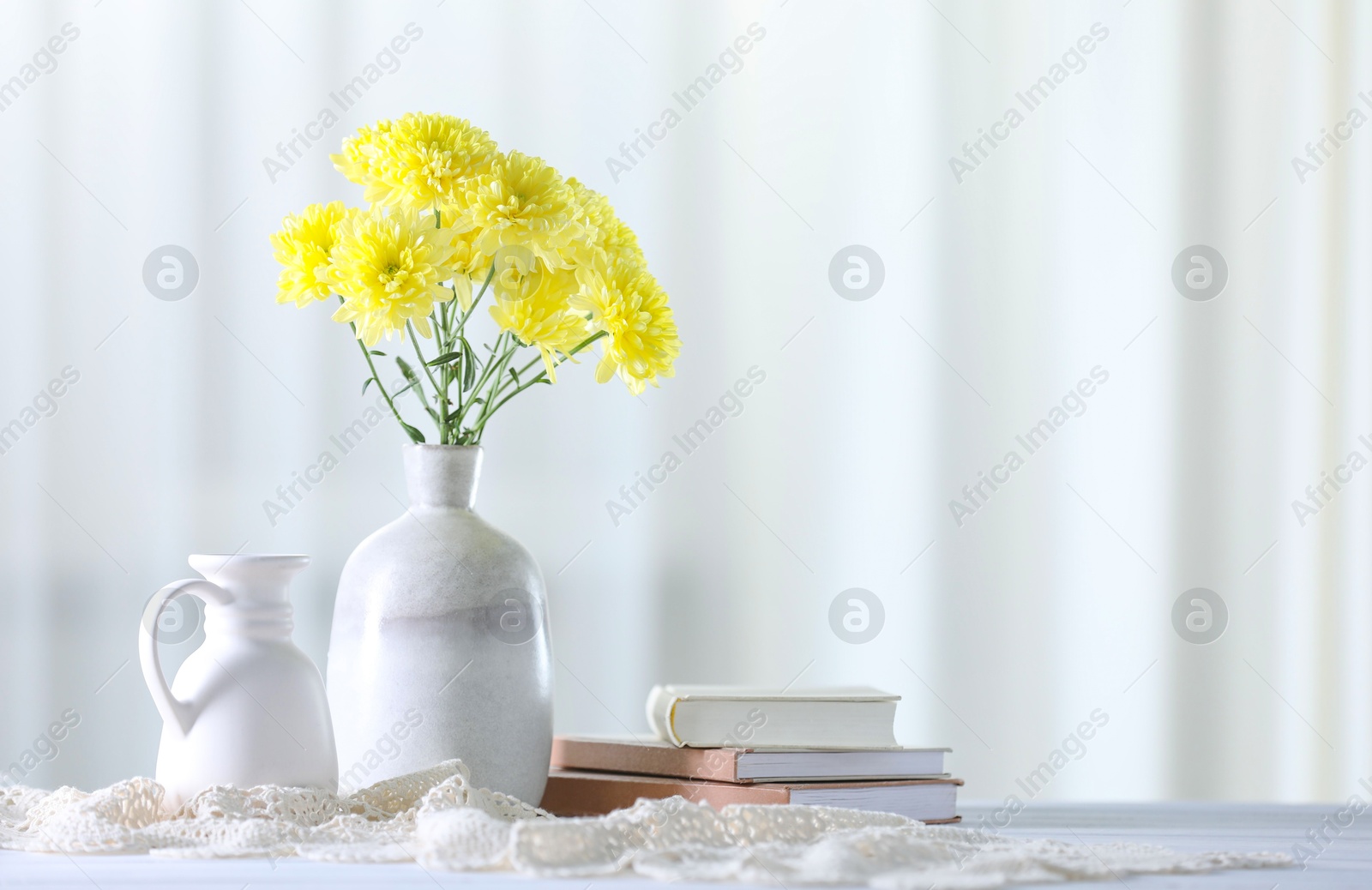 Beautiful yellow flowers in vase and books on white wooden table at home. Space for text Photo of Beautiful yellow flowers in vase and books on white wooden table at home. Space for text