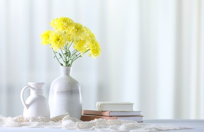 Photo of Beautiful yellow flowers in vase and books on white wooden table at home. Space for text