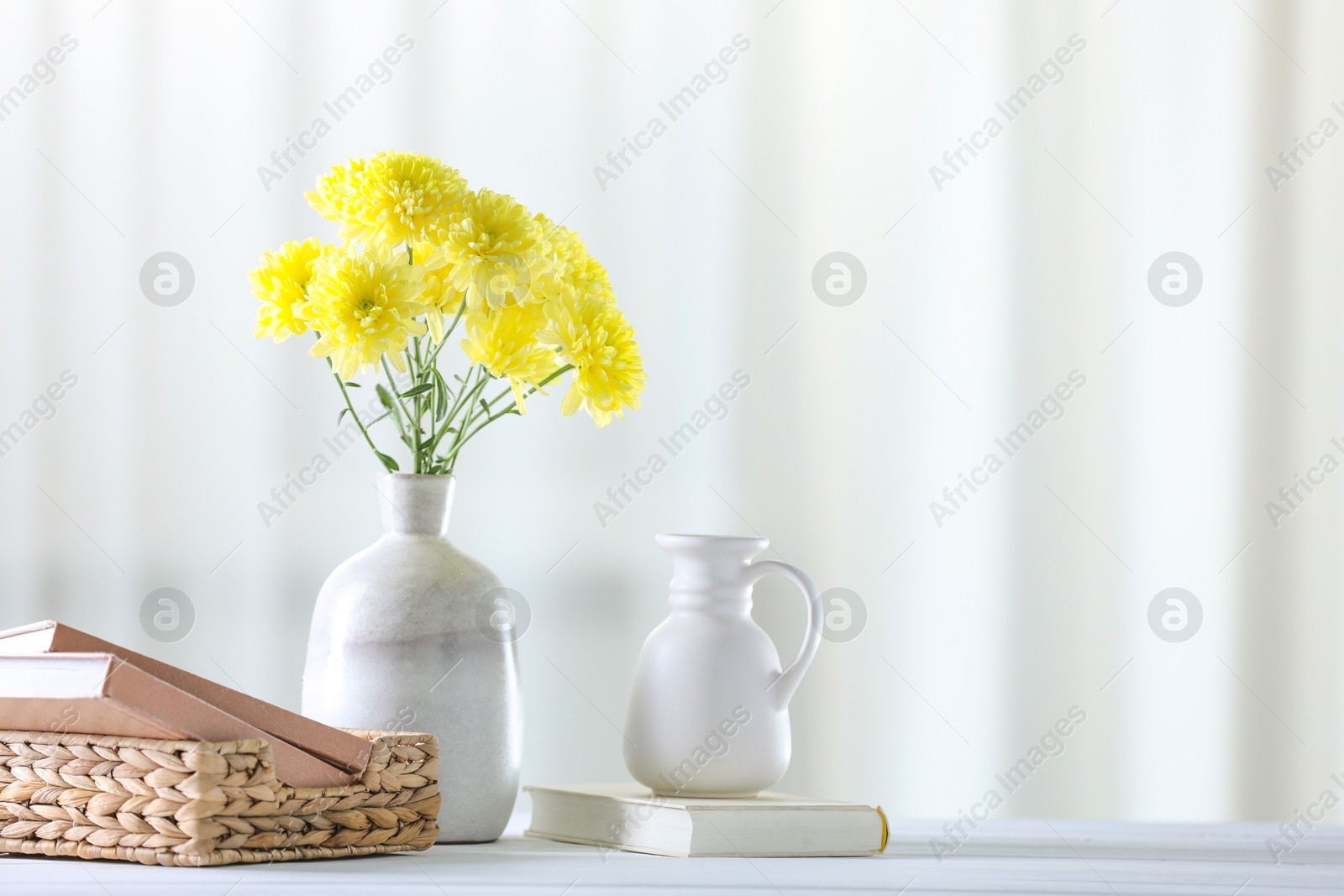 Photo of Beautiful yellow flowers in vase and books on white wooden table at home. Space for text