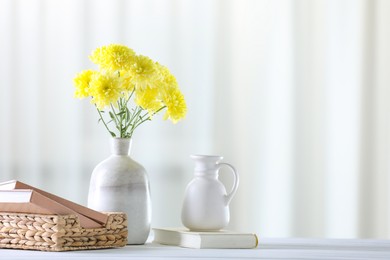 Photo of Beautiful yellow flowers in vase and books on white wooden table at home. Space for text