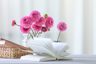 Photo of Beautiful pink flowers in vases and books on white wooden table at home, selective focus