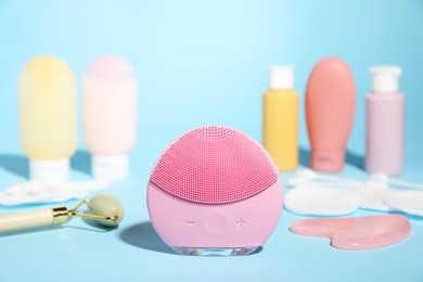 Photo of Facial cleansing brush and other skin care products on light blue background