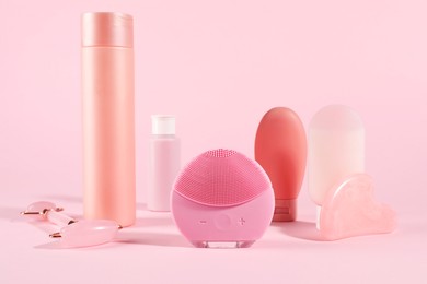 Photo of Facial cleansing brush and other skin care products on pink background