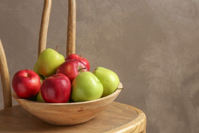 Photo of Ripe red and green apples in bowl on wooden chair near grey wall. Space for text