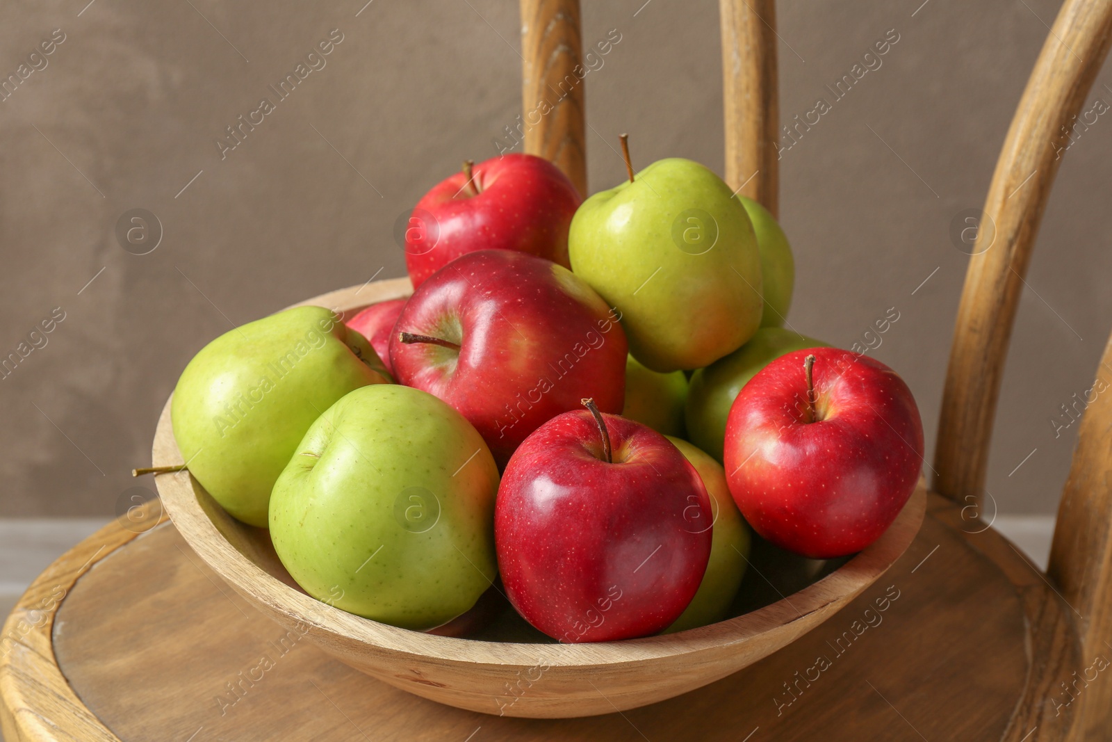 Photo of Ripe red and green apples in bowl on wooden chair near grey wall, closeup