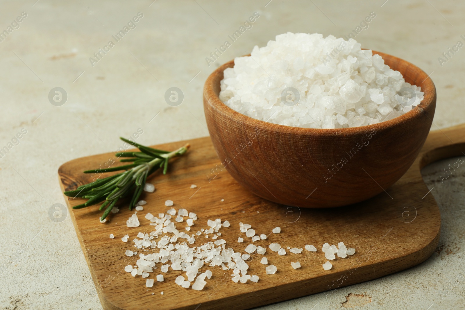 Photo of Sea salt in bowl and rosemary on grey table, closeup