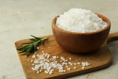 Photo of Sea salt in bowl and rosemary on grey table, closeup