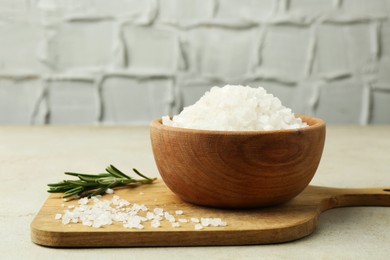 Photo of Sea salt in bowl and rosemary on grey table, closeup