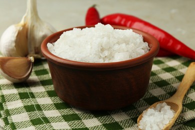 Photo of Sea salt in bowl, garlic and chili peppers on table, closeup