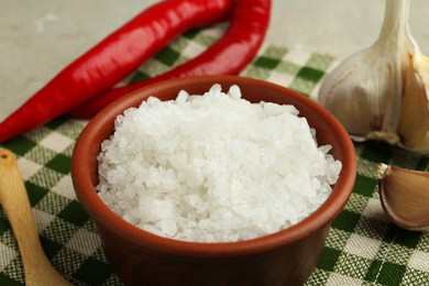 Photo of Sea salt in bowl, garlic and chili peppers on table, closeup