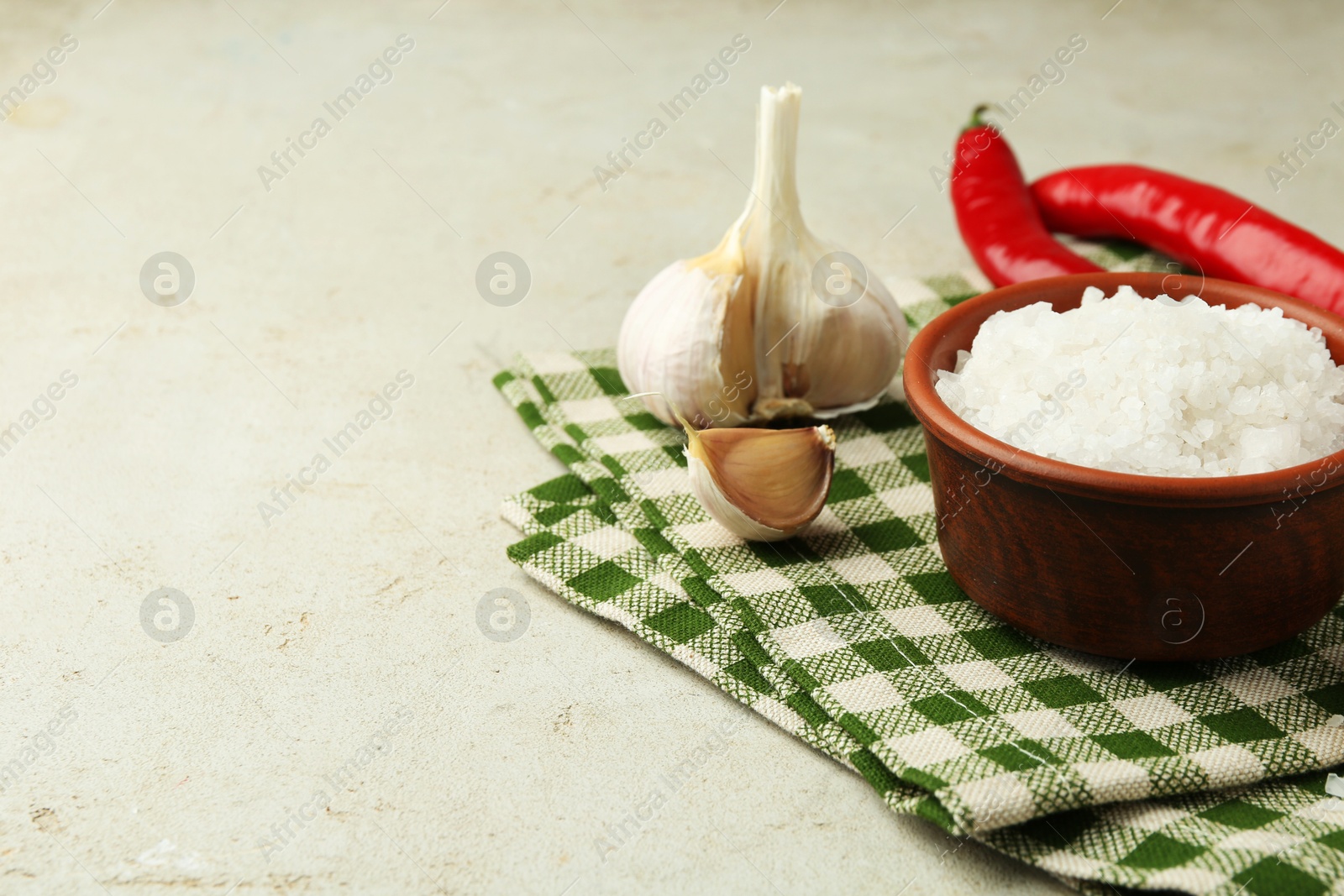 Photo of Sea salt in bowl, garlic and chili peppers on grey table, closeup. Space for text