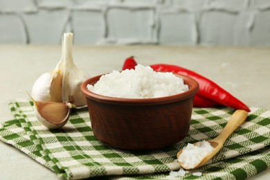 Photo of Sea salt in bowl, garlic and chili peppers on grey table, closeup