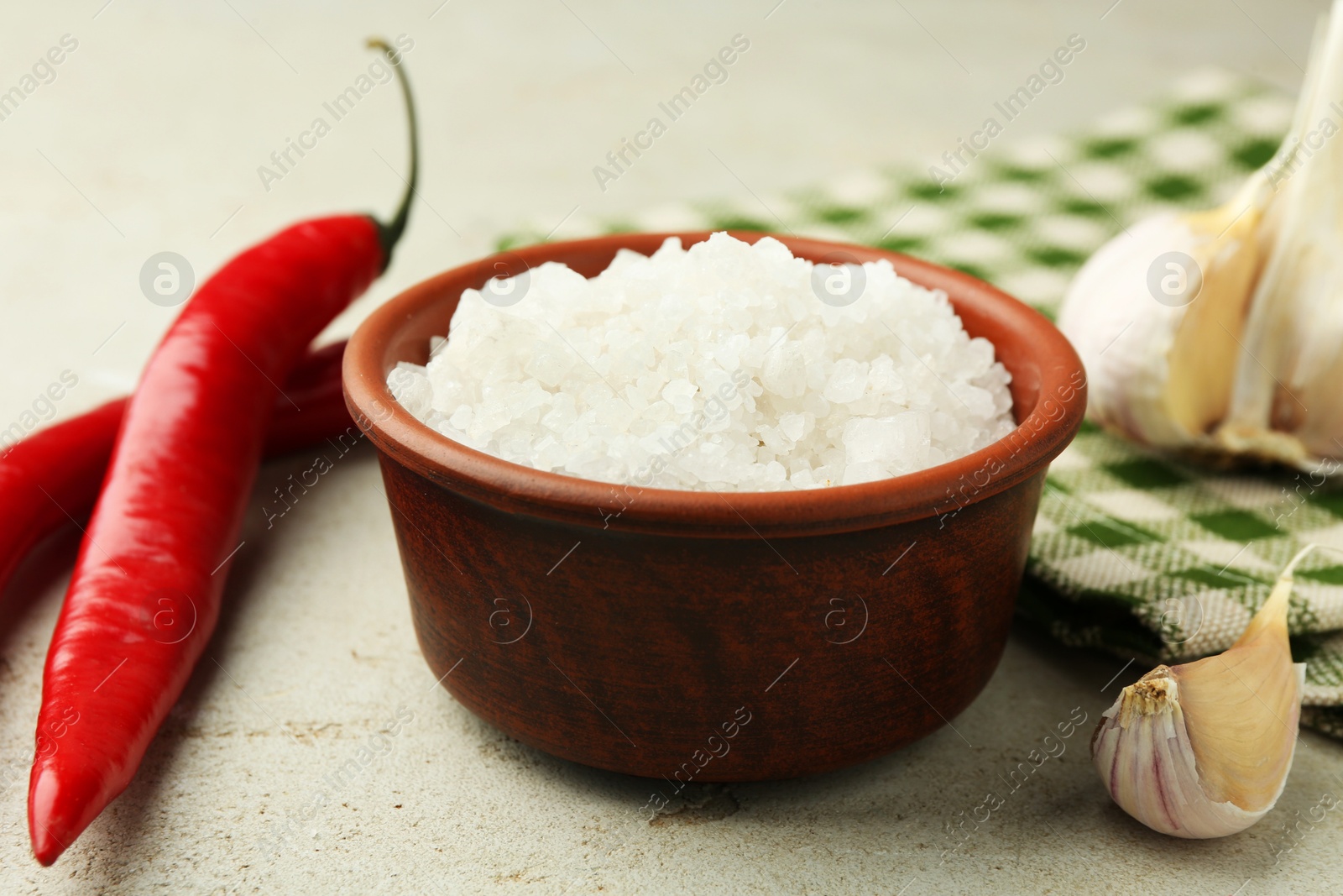 Photo of Sea salt in bowl, garlic and chili peppers on grey table, closeup