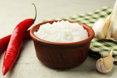 Photo of Sea salt in bowl, garlic and chili peppers on grey table, closeup