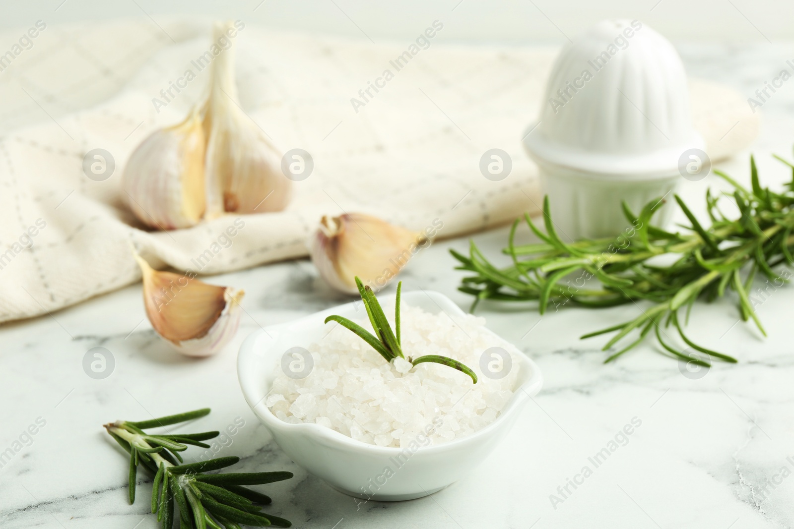 Photo of Sea salt, rosemary and garlic on white marble table, closeup