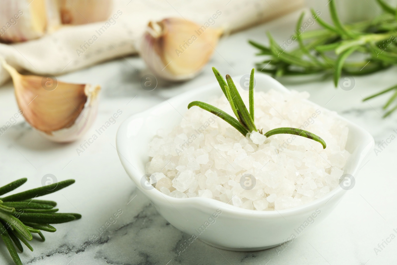 Photo of Sea salt, rosemary and garlic on white marble table, closeup