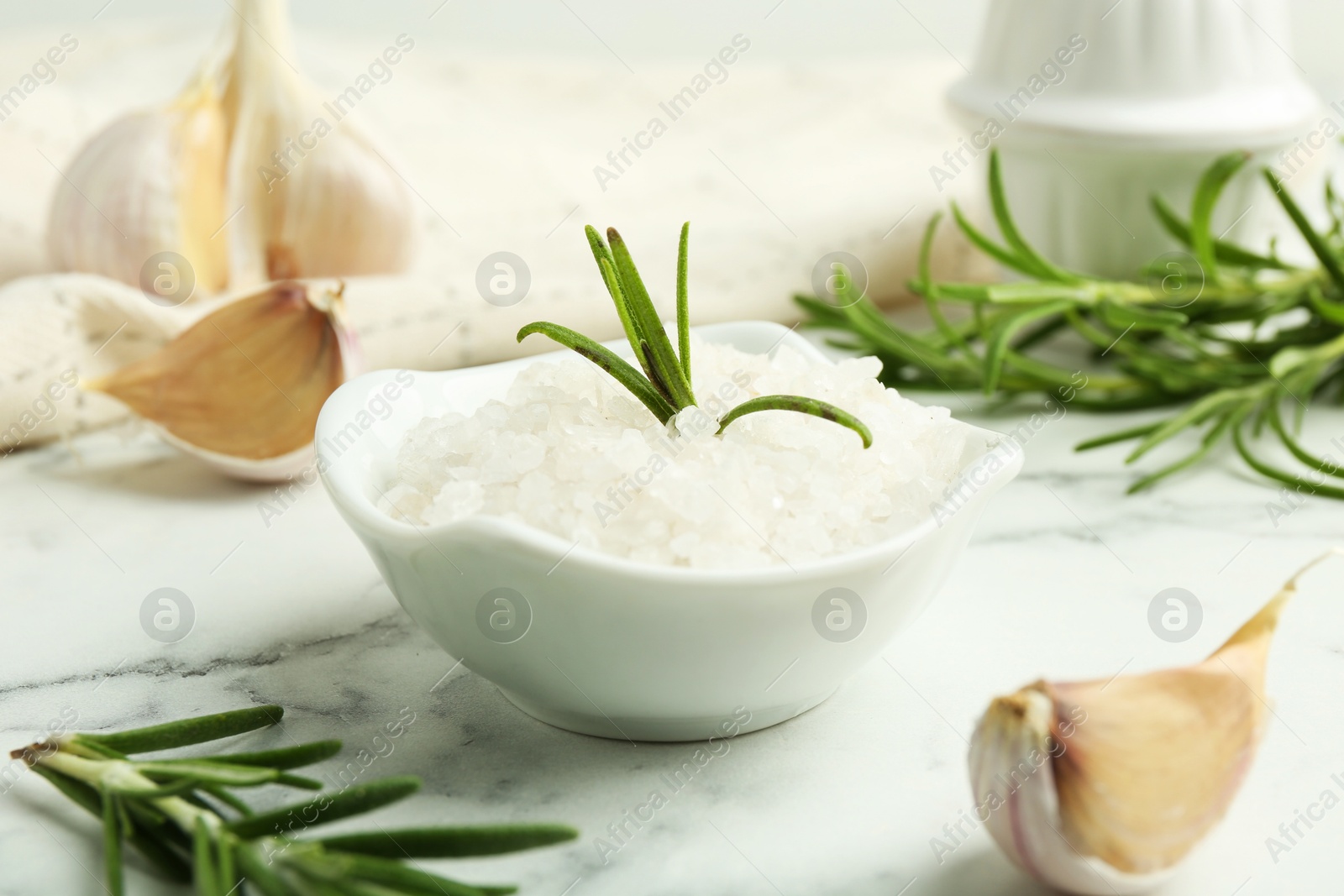 Photo of Sea salt, rosemary and garlic on white marble table, closeup