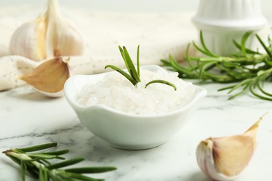 Photo of Sea salt, rosemary and garlic on white marble table, closeup