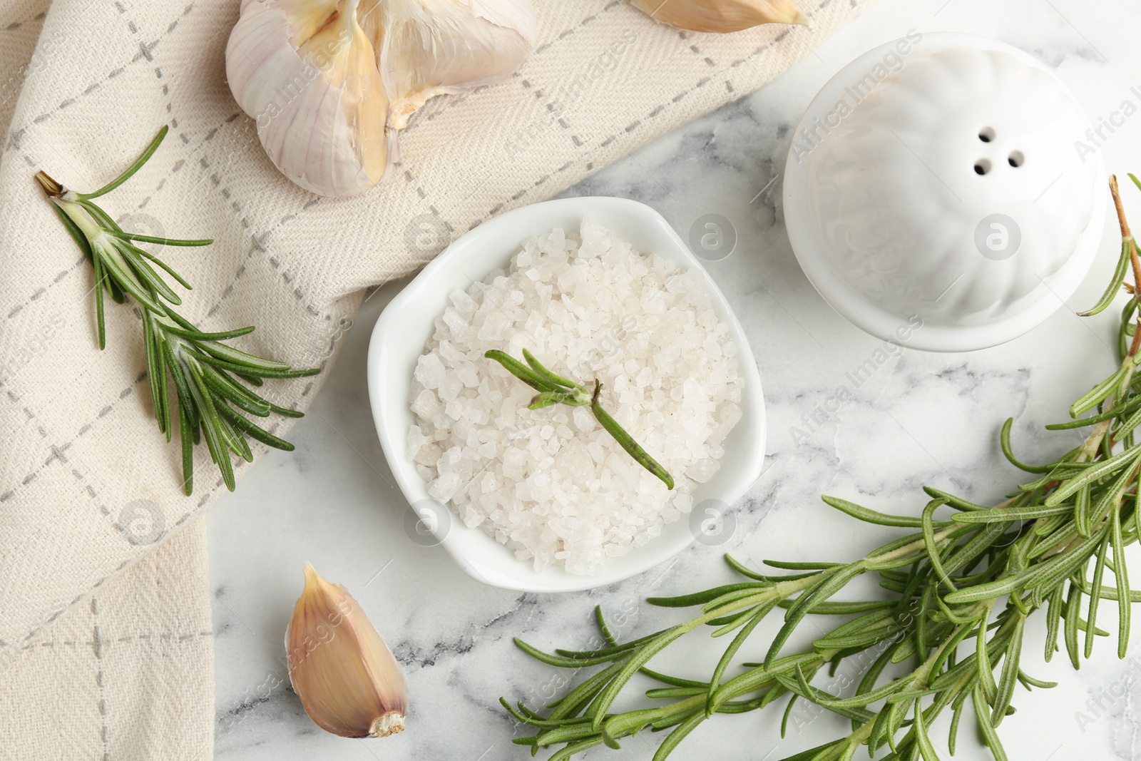 Photo of Sea salt, rosemary and garlic on white marble table, top view