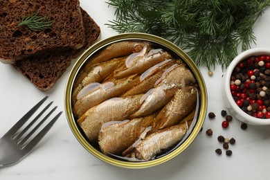 Photo of Tasty sprats in tin can, dill, bread and peppercorns on white marble table, top view